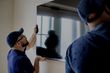 two handymen mounting a tv onto a wall 